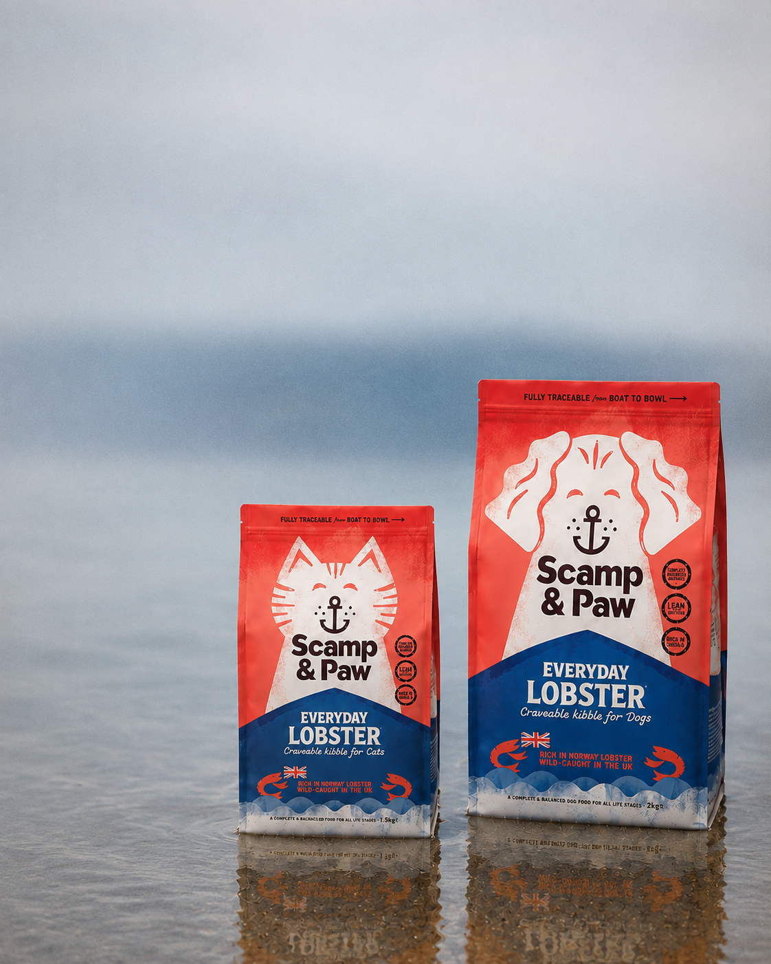 Two bags of Scamp & Paw Everyday Lobster canned fish wet cat food stand on wet sand with a blurred beach and ocean background.
